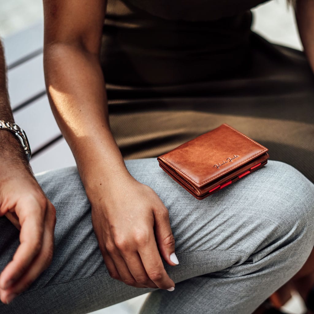 High-quality leather wallet lies on the leg of a man. The hand of a woman is next to it